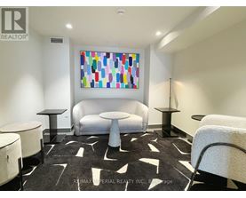 A white couch sits in a room with a colorful painting on the wall.