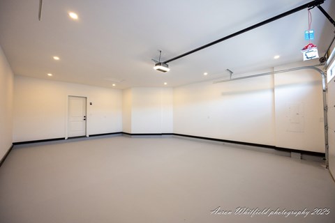A spacious room with a door on the left and a wall-mounted light fixture on the right.