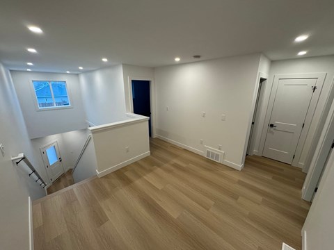 A room with wooden flooring and white walls, featuring a staircase and a window.
