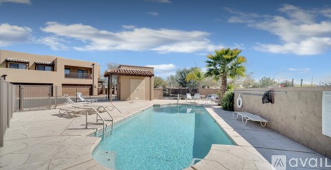 A pool in a backyard with a patio and a building in the background.