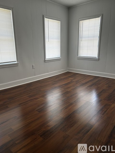 A room with wooden flooring and two windows.