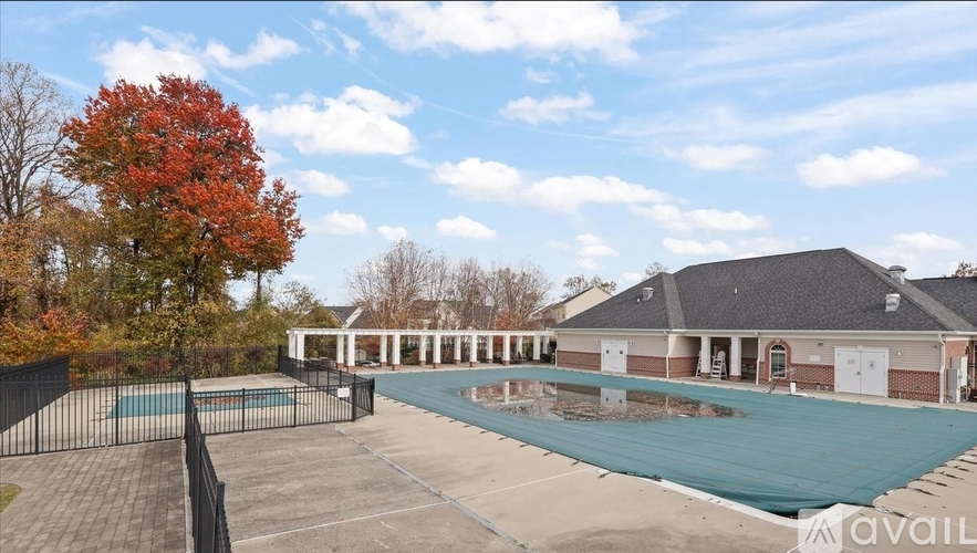 A large outdoor swimming pool surrounded by a black fence and a red tree.
