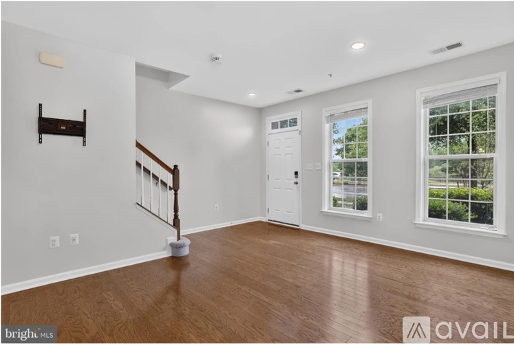 A spacious room with wooden floors and white walls, featuring a staircase with a wooden railing.