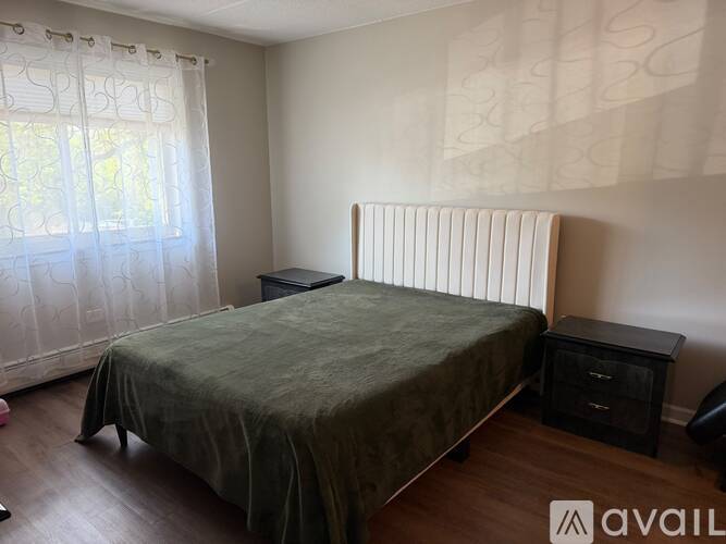 A bedroom with a bed, nightstand, and window with curtains.