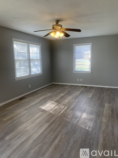 A room with a ceiling fan and two windows.