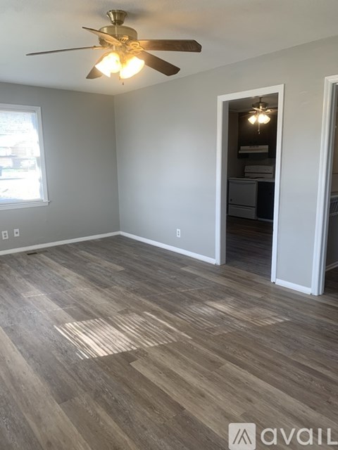 A room with a ceiling fan and light fixture, and a doorway leading to another room.