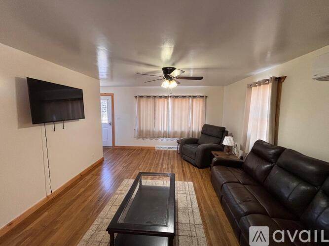 A living room with a black leather couch and a flat screen TV mounted on the wall.