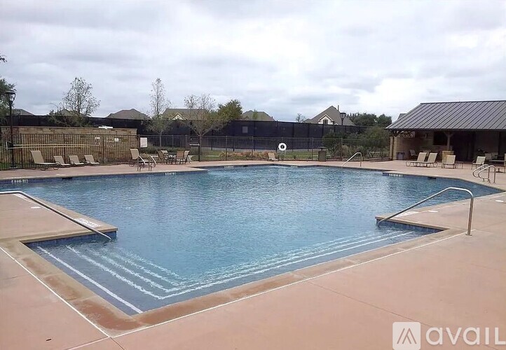 A large outdoor swimming pool with a fence and a small building in the background.