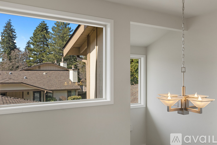 A modern chandelier hangs in a well-lit room with a view of a house and trees outside the window.