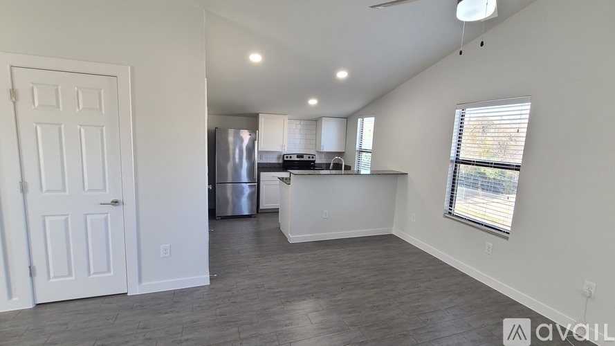 A spacious kitchen and living room with a refrigerator, microwave, and a window with blinds.