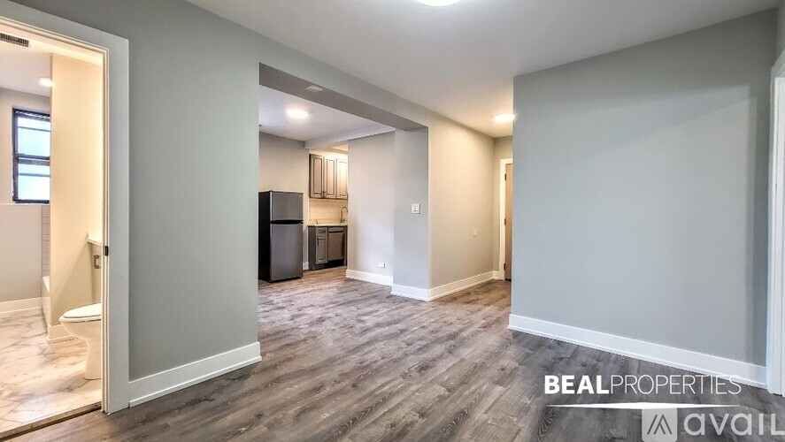 A spacious room with a doorway leading to another room, a window on the left, and a fridge in the corner.