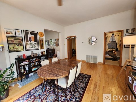A living room with a wooden table and chairs, a bookshelf, and a Barclays Lager poster on the wall.