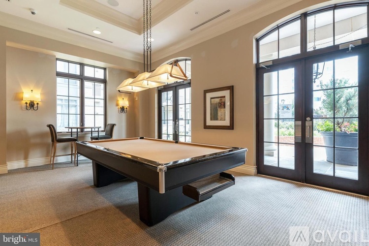 A pool table is in the middle of a room with a chair and a window.