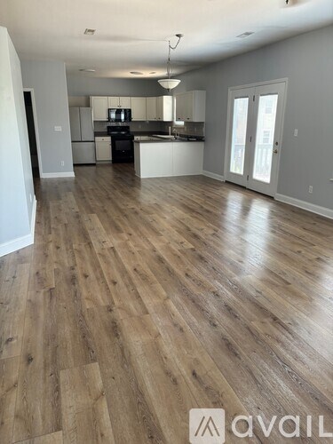 A spacious room with wooden flooring and a kitchen area in the background.
