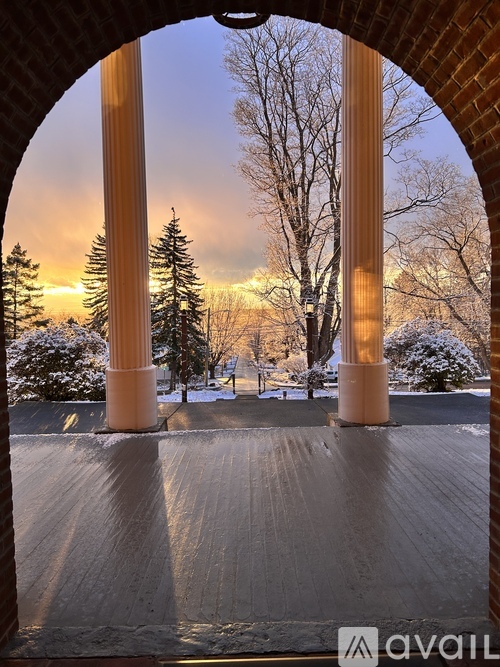 A view through an archway looking out to a snowy landscape with trees and a sunset.