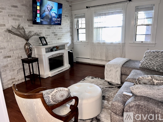 A living room with a white brick wall and a television mounted above a fireplace.