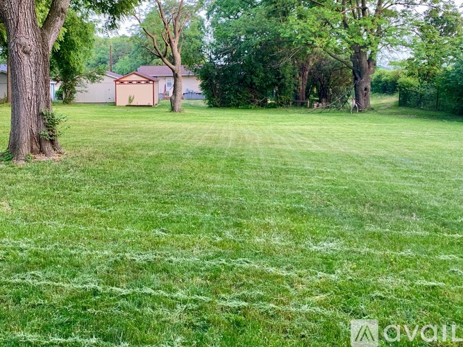 A grassy field with trees and a house in the background.