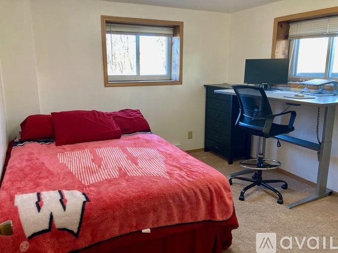 A bedroom with a red bedspread and a black desk with a computer.