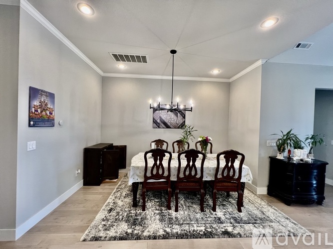 A dining room with a black and white rug, a wooden table and chairs, and a chandelier.