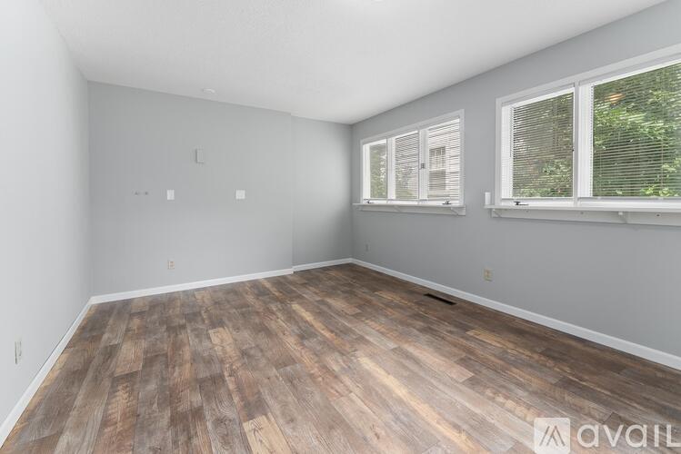 A room with wooden flooring and two windows.