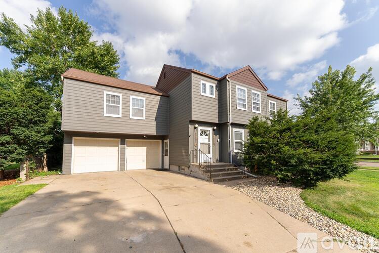 A two-story house with a garage is surrounded by trees and has a driveway leading to the front door.