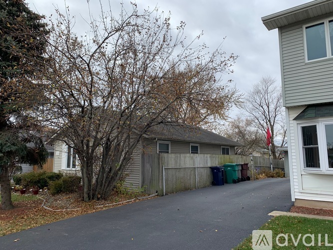 A tree with no leaves stands in front of a grey house.