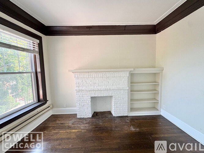 A white fireplace in a room with wooden floors and a window.