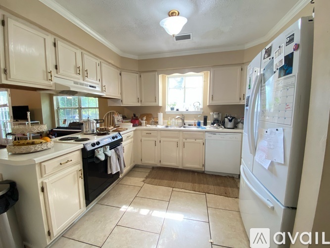 A kitchen with white cabinets and appliances, a refrigerator with a calendar on it, and a window letting in natural light.