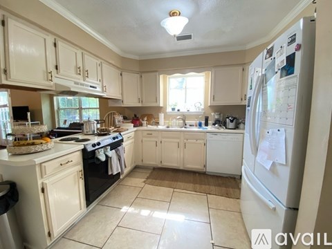 A kitchen with white cabinets and appliances, a refrigerator with a calendar on it, and a window letting in natural light.