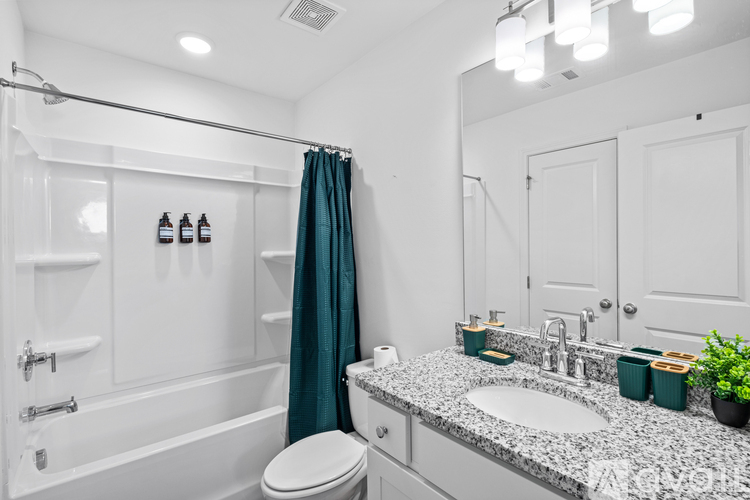 A white bathroom with a white tub and toilet, a sink with a mirror above it, and a green plant on the counter.