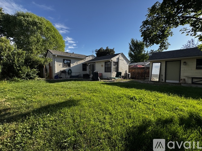 A grassy area with a few houses and trees in the background.