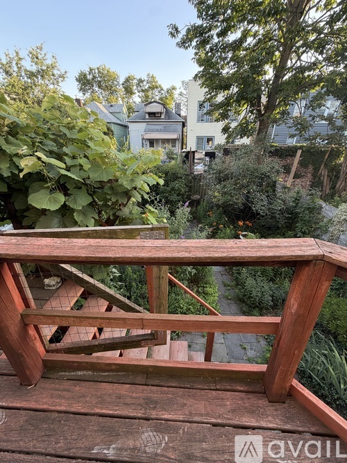 A wooden deck with a railing and a view of a garden and buildings in the background.