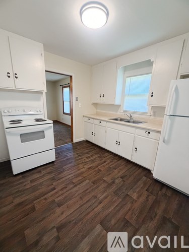 A kitchen with white appliances and wooden floors.