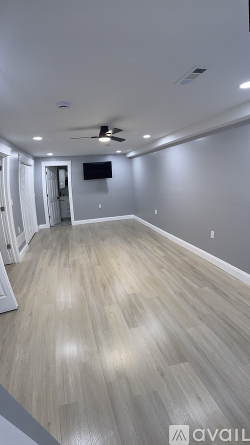 A spacious room with light wood flooring and a ceiling fan.