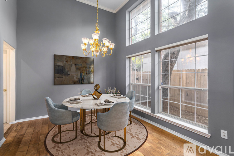A dining room with a round table and chairs, a chandelier, and a view of a fence outside the window.