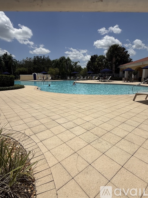A large outdoor swimming pool surrounded by a tiled patio and lounge chairs.