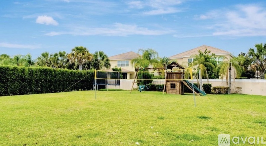 A grassy area with a house and a playground in the background.