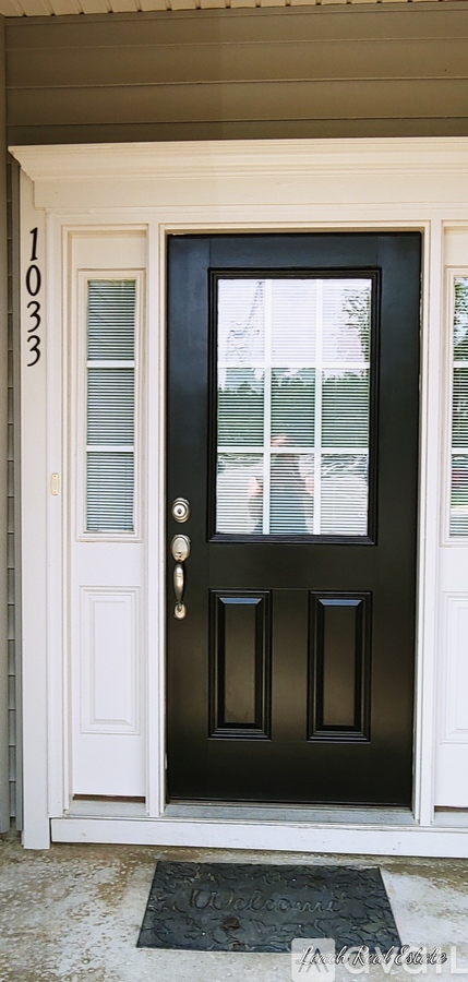 A black door with a glass window and a doormat that says "Welcome".