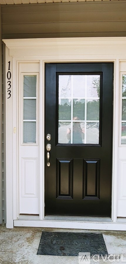 A black door with a glass window and a doormat that says "Welcome".