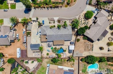 A bird's eye view of a residential area with houses, a pool, and a dirt road.