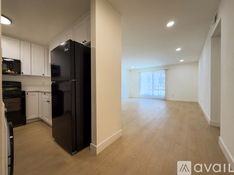 A black refrigerator in a kitchen with wooden floors and white cabinets.