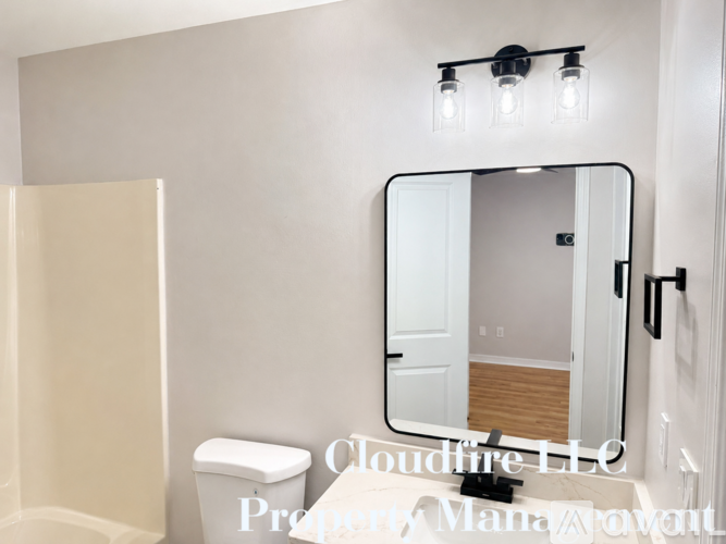 A bathroom with a toilet, a mirror, and lights above it.