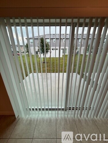 A view through a window with blinds looking out to a grassy area and buildings.