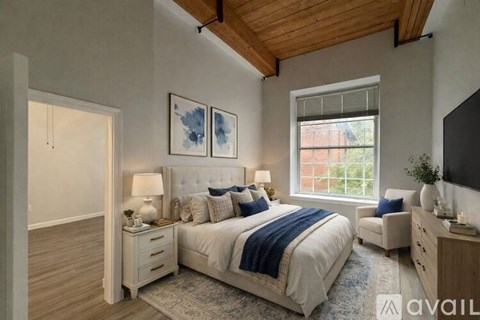 A bedroom with a large bed, a window, and a wooden ceiling.