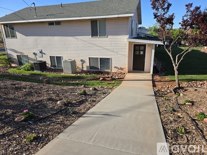 A house with a grey siding and a brown door is shown with a concrete walkway leading to it.