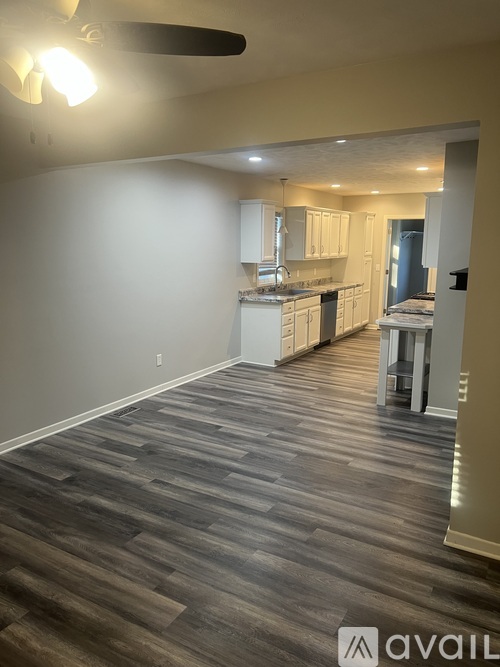A room with a kitchen in the background and a wooden floor.