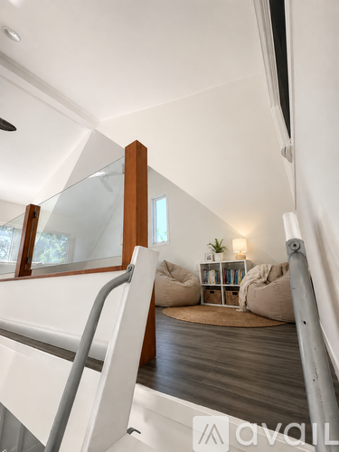 A white staircase with a glass railing leads to a living room with a couch and a small table.