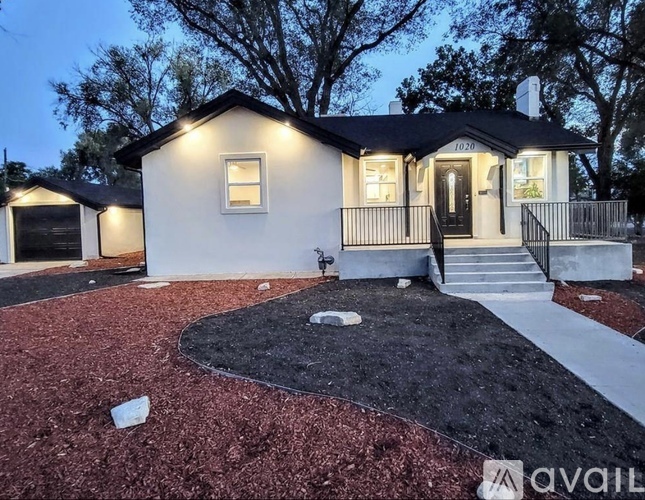 A house with a black roof and white walls is surrounded by a red mulch.