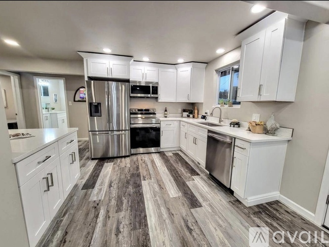 A modern kitchen with white cabinets and a wooden floor.
