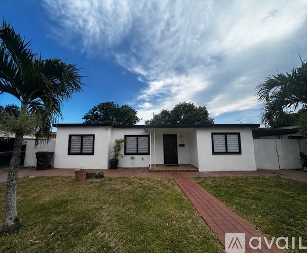 A house with a black door and windows is surrounded by a grassy area and palm trees.